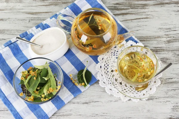 Kettle and cup of tea with linden on wooden table — Stock Photo, Image