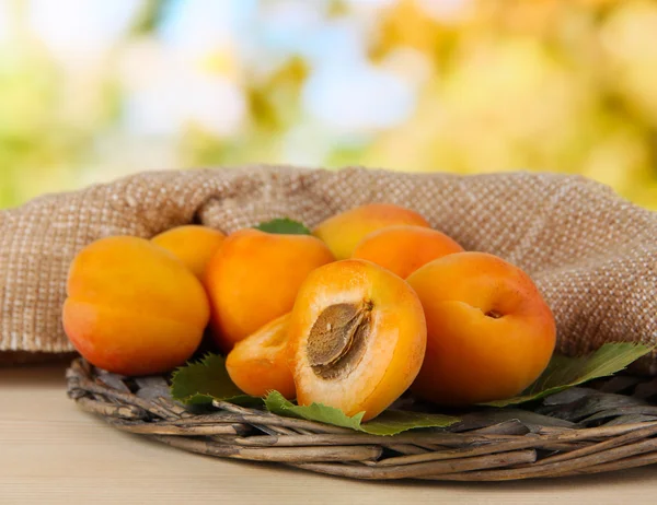 Apricots on wicker coasters on wooden table on nature background — Stock Photo, Image