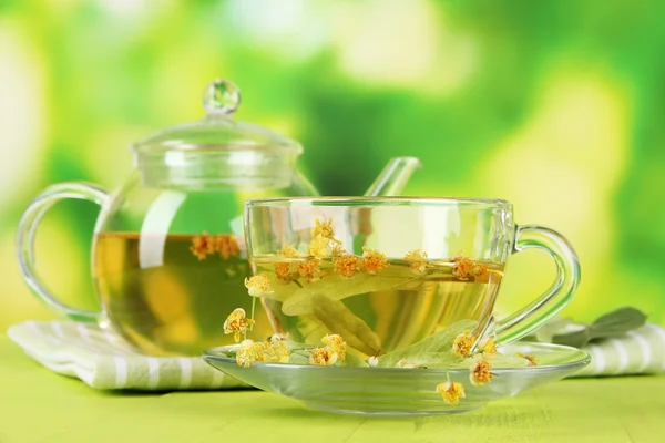 Kettle and cup of tea with linden on wooden table on nature background — Stock Photo, Image