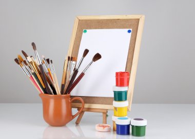 Small easel with sheet of paper and art supplies isolated on white clipart