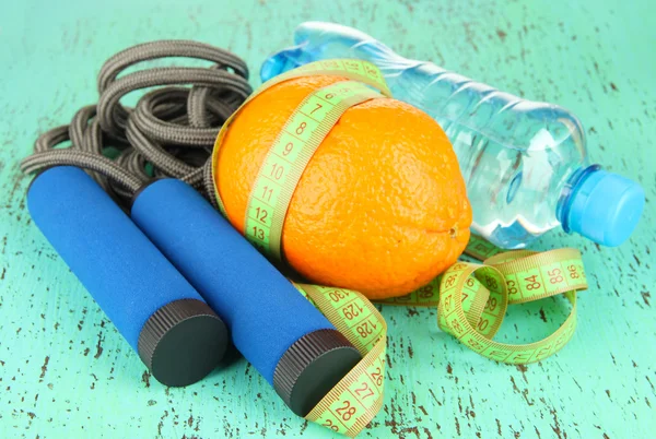 Orange with measuring tape,skipping rope and bottle of water, on color wooden background — Stock Photo, Image