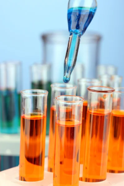 Лабораторная пипетка с каплей цветной жидкости над стеклянными пробирками, крупным планом — стоковое фото