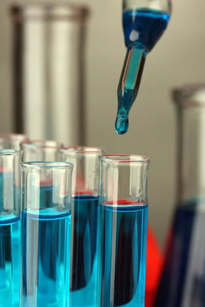 Pipeta de laboratorio con gota de líquido de color sobre tubos de ensayo de vidrio, primer plano —  Fotos de Stock