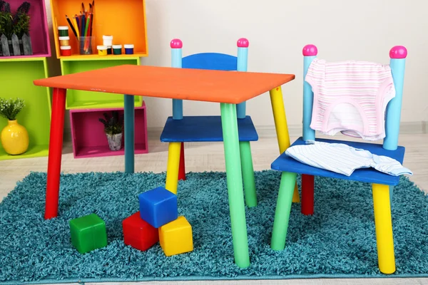 Mesa pequena e colorida e cadeiras com roupas de bebê — Fotografia de Stock