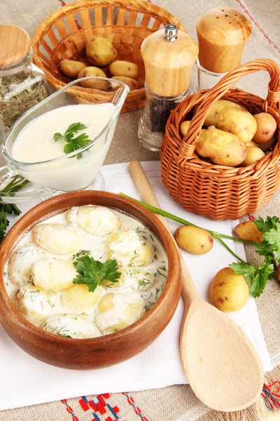 Tender batatas jovens com creme de leite e ervas em tigela de madeira na toalha de mesa close-up — Fotografia de Stock