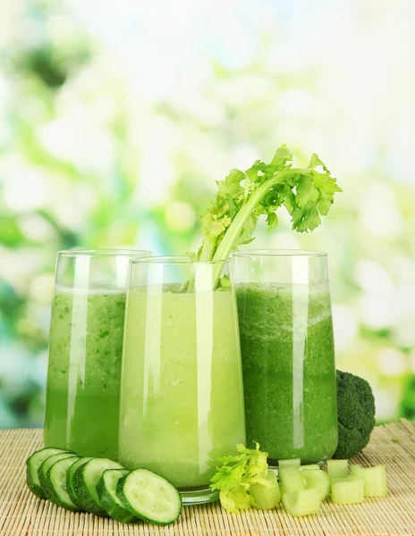 Glasses of green vegetable juice on bamboo mat, on green background — Stock Photo, Image