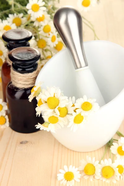 Aceite esencial y flores de manzanilla en mortero sobre mesa de madera —  Fotos de Stock