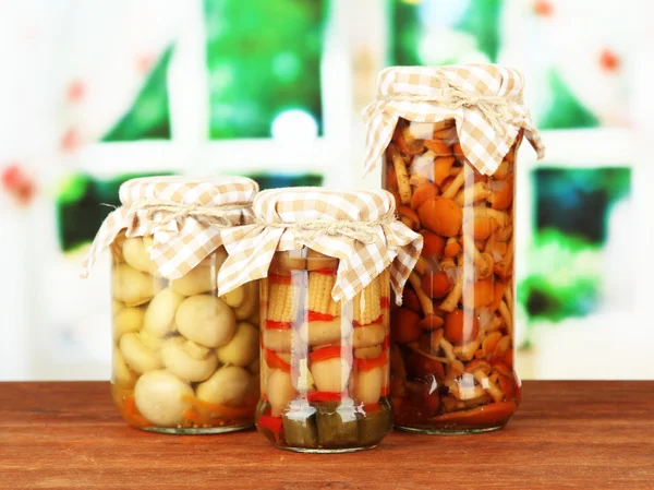 Delicious marinated mushrooms in glass jars, on wooden table on bright background — Stock Photo, Image