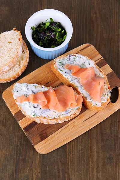 Ahşap masa üzerinde kesme tahtası üzerinde balık sandviç — Stok fotoğraf