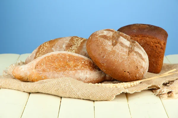 Komposisi dengan roti dan kain karung di atas meja kayu, pada latar belakang warna — Stok Foto