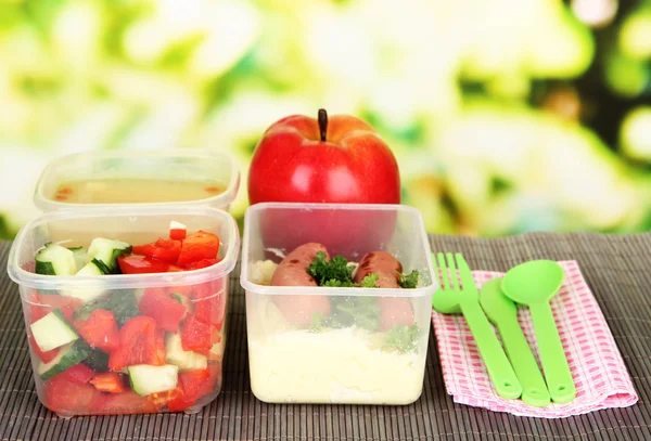 Tasty lunch in plastic containers, on bamboo mat on bright background — Stock Photo, Image