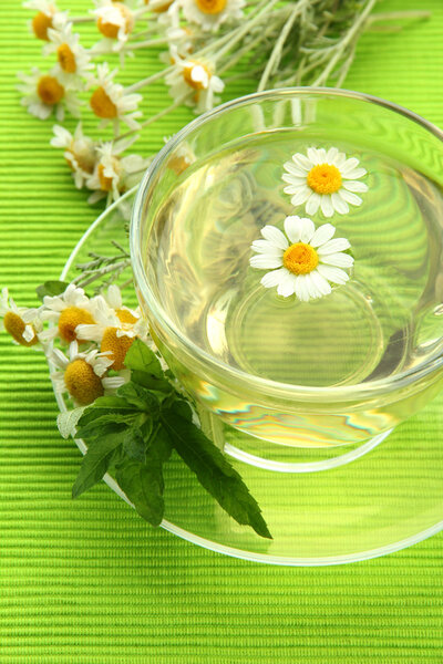 Чашка травяного чая с дикими ромашками и мятой, на зеленой салфетке
