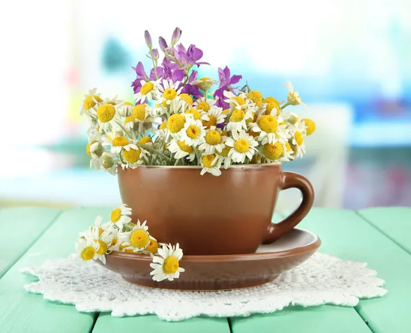 Bouquet of chamomile flowers in cup, on bright background — Stock Photo, Image