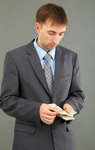 Jovem empresário com dinheiro no fundo cinzento — Fotografia de Stock