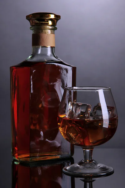 Brandy sklenice s ledem a láhev na šedém pozadí — Stock fotografie