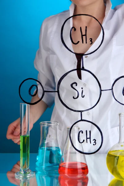 Chemist woman writing formulas on glass on blue background — Stock Photo, Image