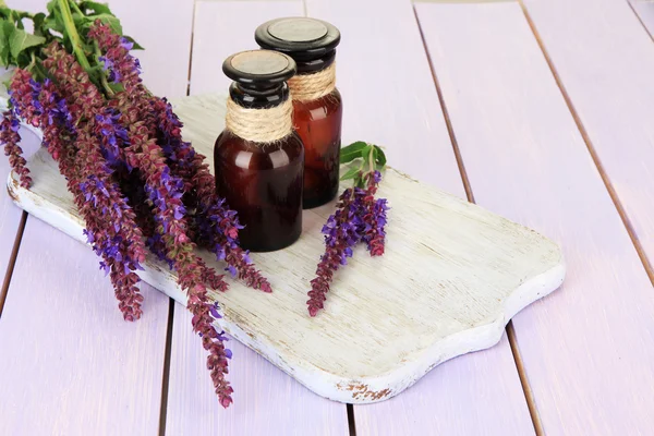 Geneeskundeflessen en salvia bloemen op paarse houten achtergrond — Stockfoto