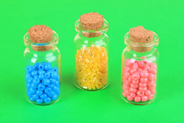 Different colorful beads in bottles on green background — Stock Photo, Image