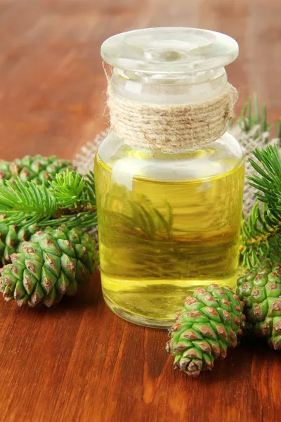 Bouteille d'huile de sapin et cônes verts sur fond bois — Photo