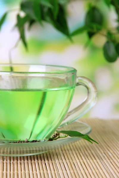 Transparante kopje groene thee op bamboe mat, op aard achtergrond — Stockfoto