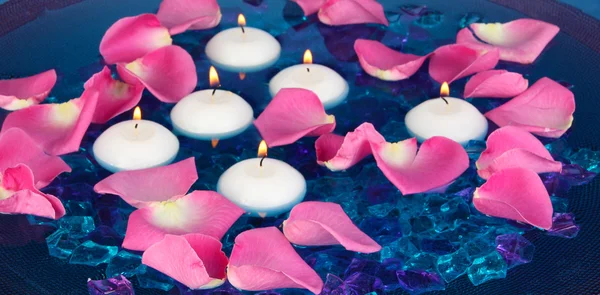 Rose petals and candles in water in vase on blue background close-up — Stock Photo, Image