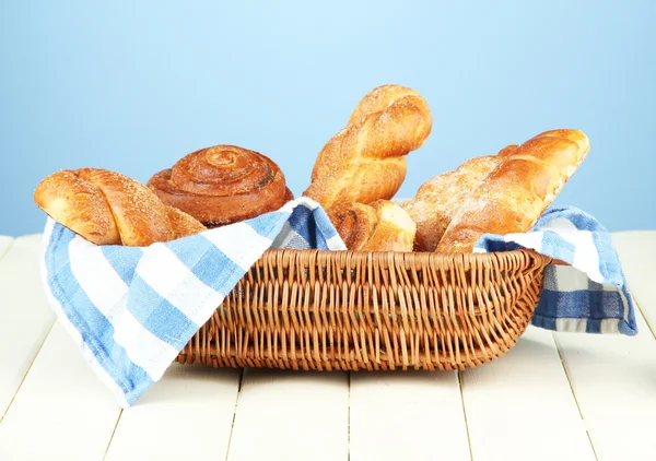 Composition with buns in wicker basket, on wooden table, on color background — Stock Photo, Image