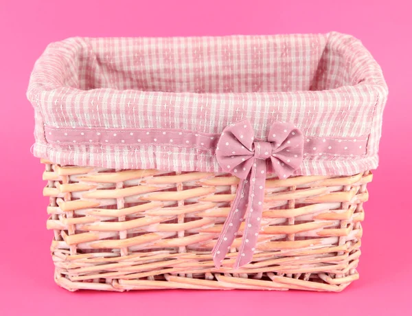 Wicket basket with pink fabric and bow, on color background — Stock Photo, Image