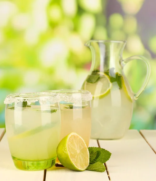 Limonata di agrumi in brocca e bicchieri su tavolo in legno su sfondo naturale — Foto Stock