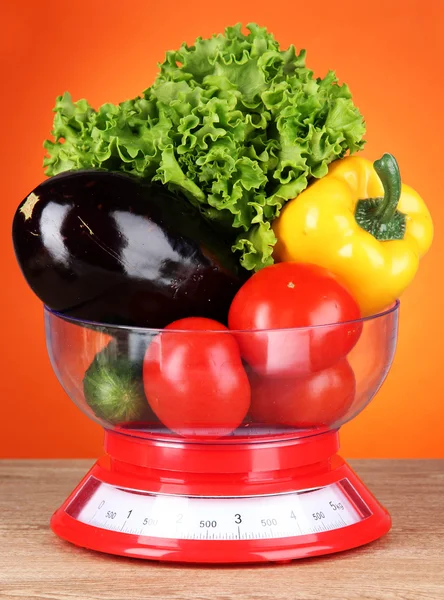 Fresh vegetables in scales on table on orange background