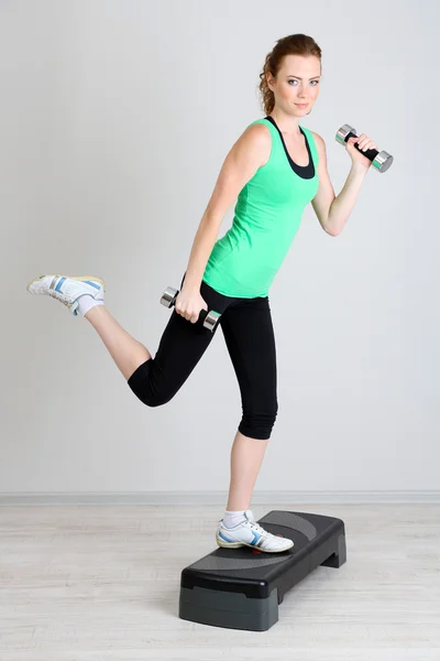 Beautiful young woman exercises with dumbbell on stepper — Stock Photo, Image