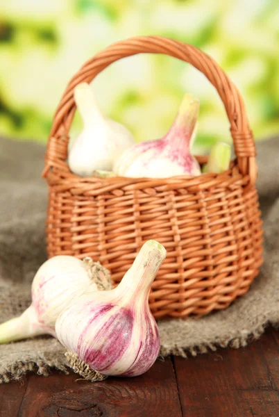 Fresh garlic in wicker basket, on sackcloth, on bright background — Stock Photo, Image