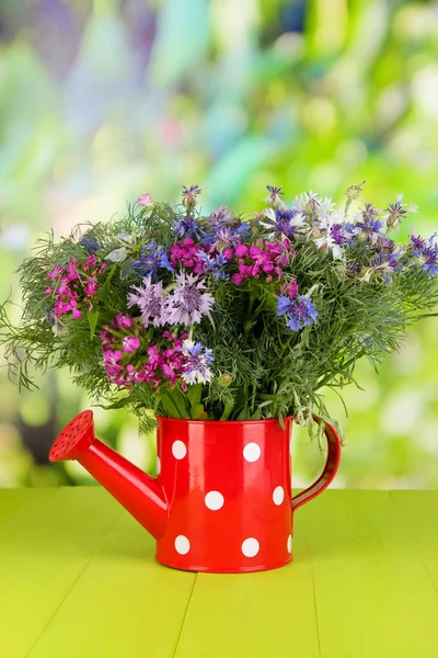 Beautiful bouquet in watering can on wooden table on natural background — Stock Photo, Image