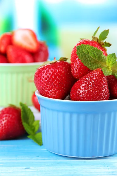 Rijpe zoete aardbeien in kommen op blauwe houten tafel — Stockfoto