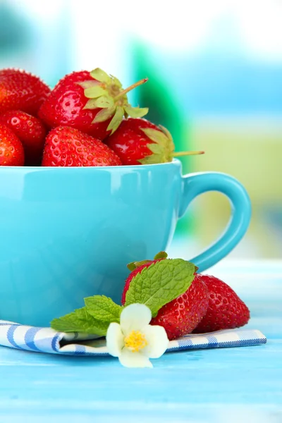 Ripe sweet strawberries in cup on blue wooden table — Stock Photo, Image