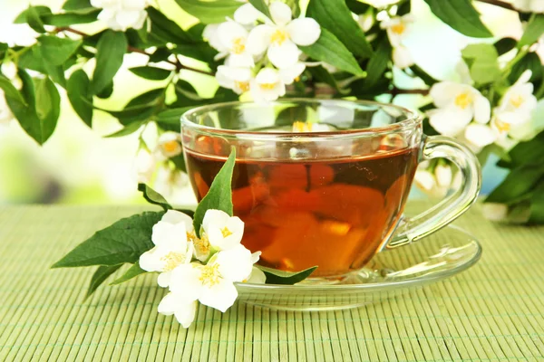 Taza de té con jazmín, sobre estera de bambú, sobre fondo brillante —  Fotos de Stock