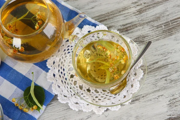 Kettle and cup of tea with linden on wooden table — Stock Photo, Image