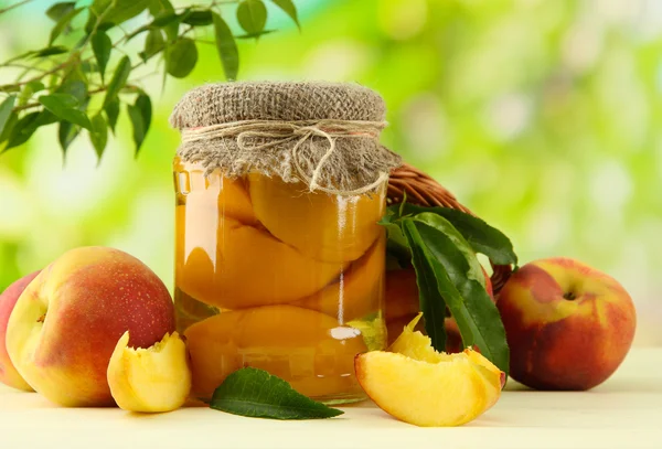 Jar of canned peaches and fresh peaches on wooden table, outside — Stock Photo, Image