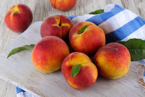 Peaches on board on napkin on table on wooden background — Stock Photo, Image