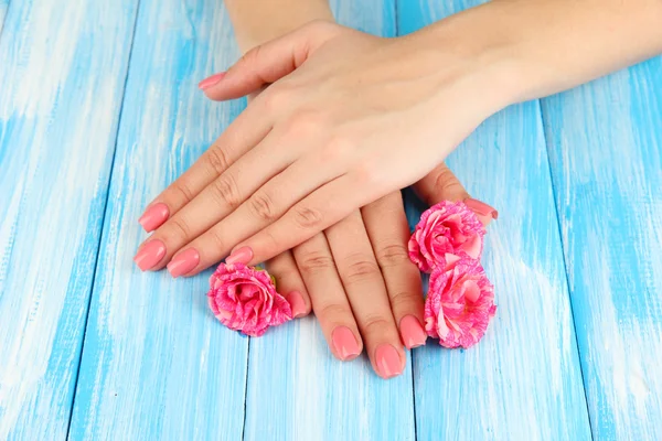 Mãos de mulher com manicure rosa e flores, na cor de fundo de madeira — Fotografia de Stock