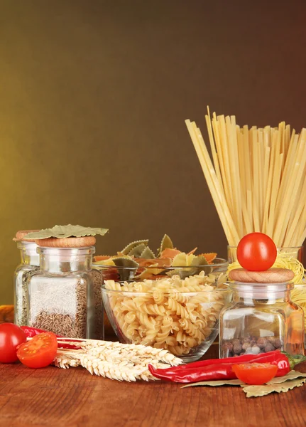 Différents types de pâtes, épices, tomates sur une table en bois — Photo