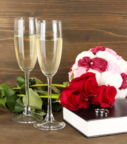 Wedding rings on bible with roses and glasses of champagne on wooden background — Stock Photo, Image