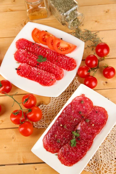 Leckere Salami auf Tellern auf Holztisch in Großaufnahme — Stockfoto