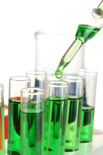 Pipeta de laboratorio con gota de líquido de color sobre tubos de ensayo de vidrio, de cerca, aislado en blanco —  Fotos de Stock