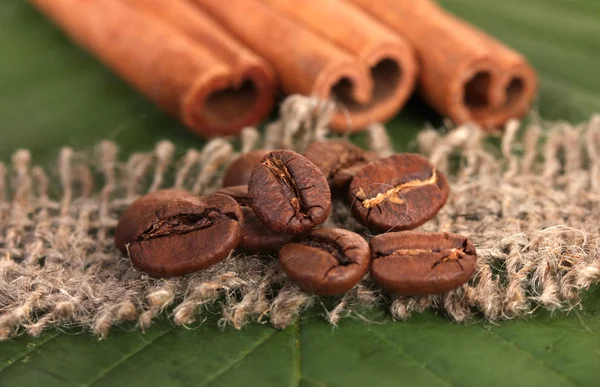 Chicchi di caffè e cannella su sacco su foglie verdi primo piano — Foto Stock