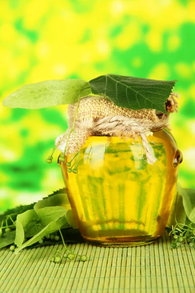 Tarro de miel con flores de lima, sobre estera de bambú de color sobre fondo brillante — Foto de Stock