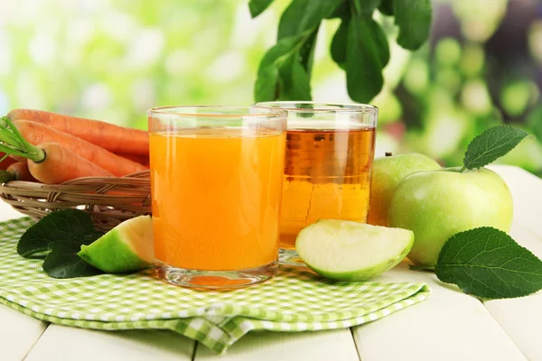 Verres de jus, pommes et carottes sur table en bois blanc, sur fond vert — Photo