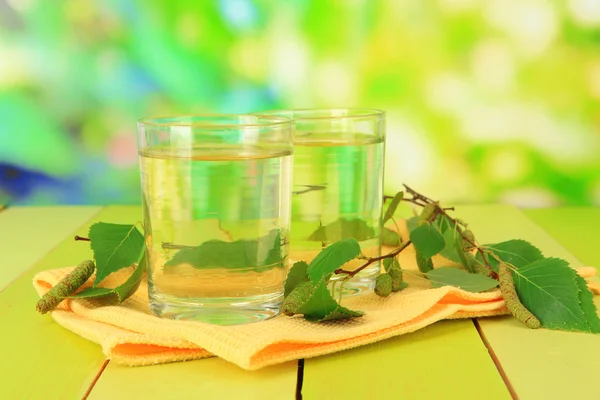 Glasses of birch sap on wooden table, on green background — Stock Photo, Image