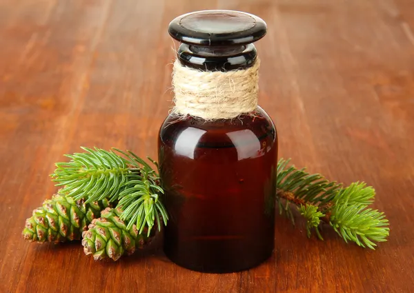 Bouteille d'huile de sapin et cônes verts sur fond bois — Photo