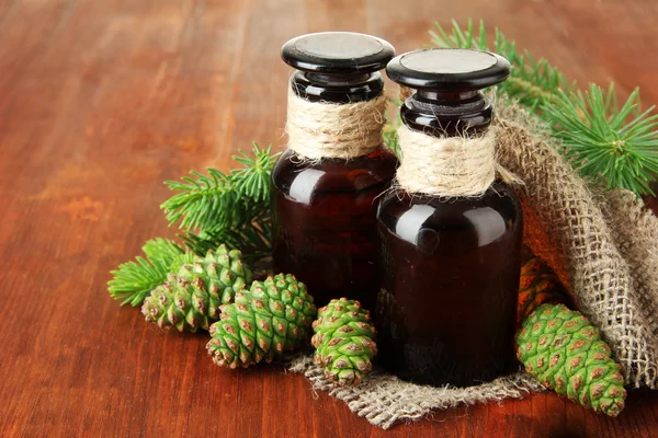 Botellas de aceite de abeto y conos verdes sobre fondo de madera — Foto de Stock