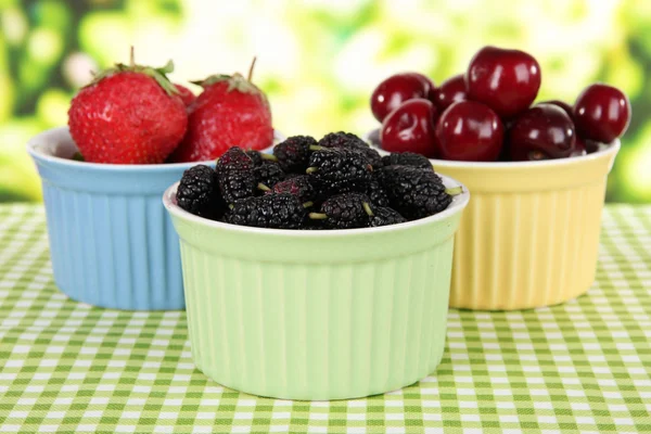 Ripe mulberries with cherry and strawberries in bowls on table on bright background — Stock Photo, Image